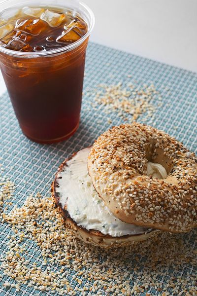 Sesame bagel with cream cheese spread in the center and a cup of iced coffee