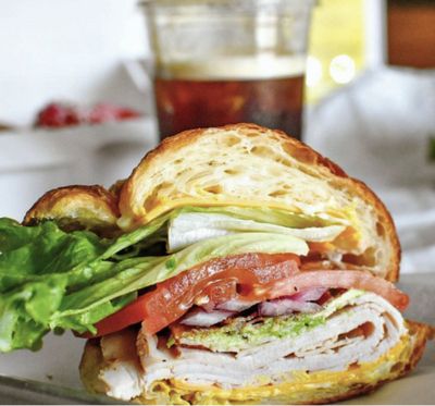 Breakfast croissant with meat, onions, tomatoes, lettuce, and avocado spread