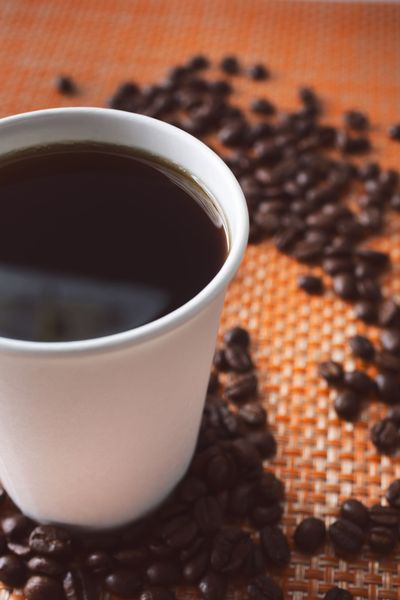 Dark coffee on an orange placemat with coffee beans