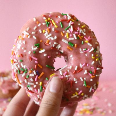 Donut with pink glaze and rainbow sprinkles being held up
