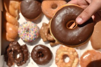 Donut with chocolate frosting being held over a variety of other pastries
